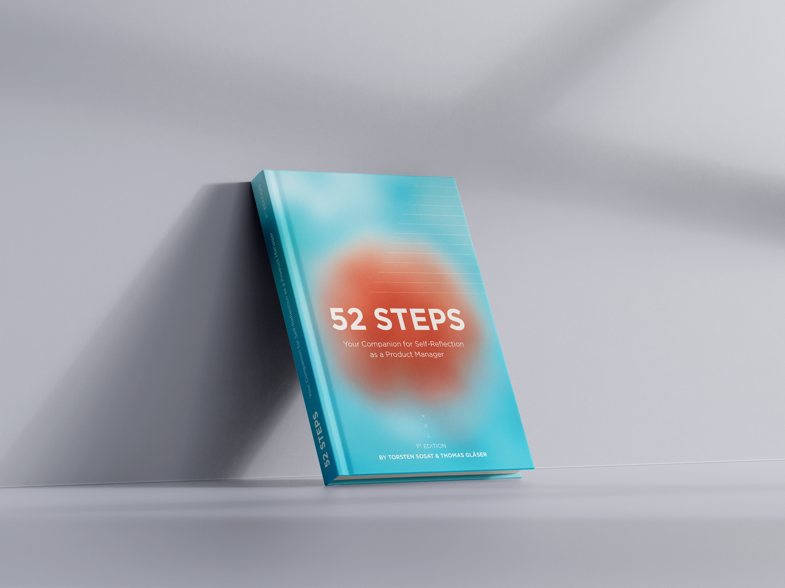 A book titled '52 STEPS: Your Companion for Self-Reflection as a Product Manager' leaning against a wall on a flat surface, with a gradient blue and orange cover design.