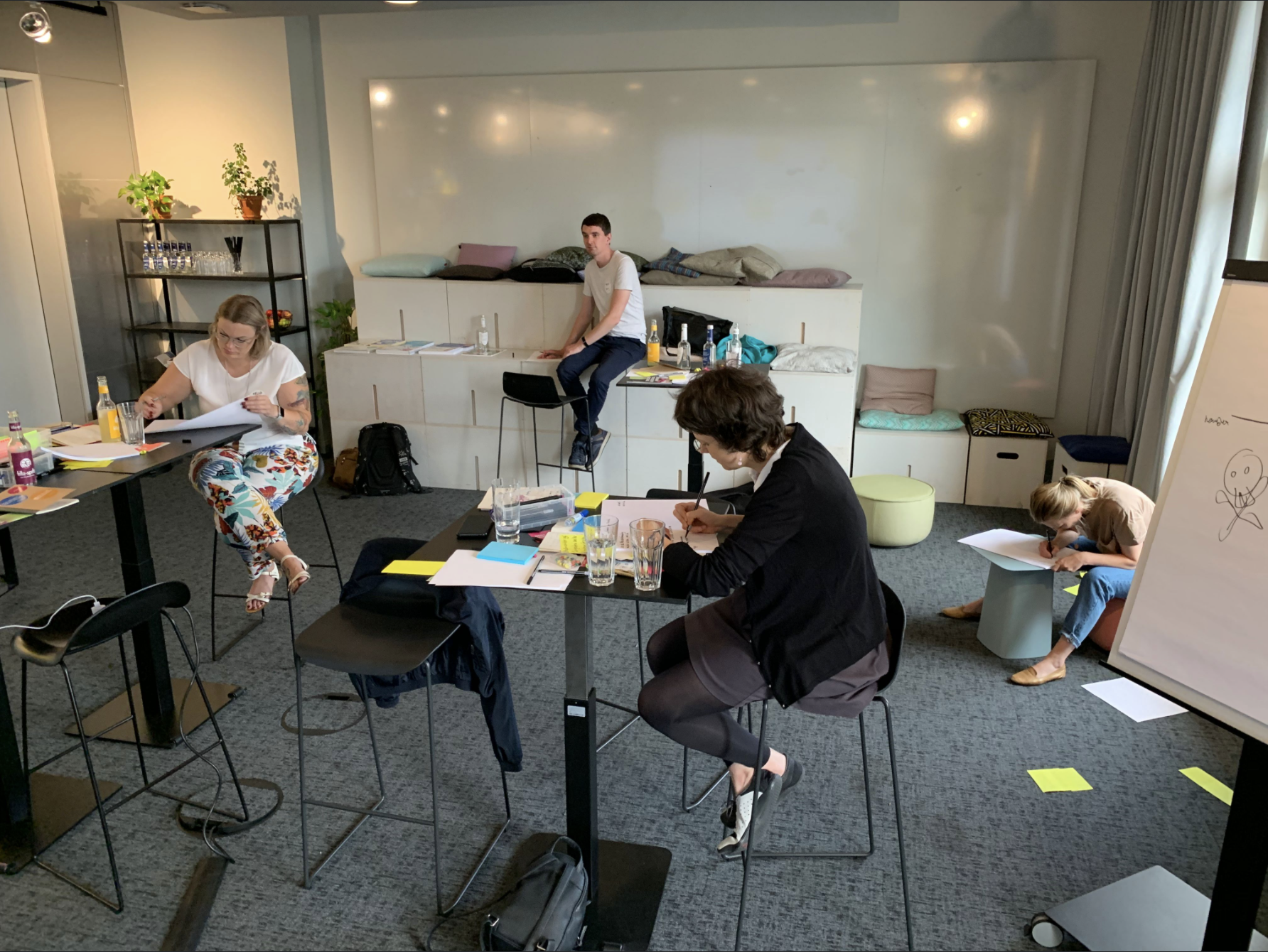 A group of five people working and studying in a modern conference room with tables, chairs, notebooks, and drinks, some are writing, and others are reading or reviewing papers.