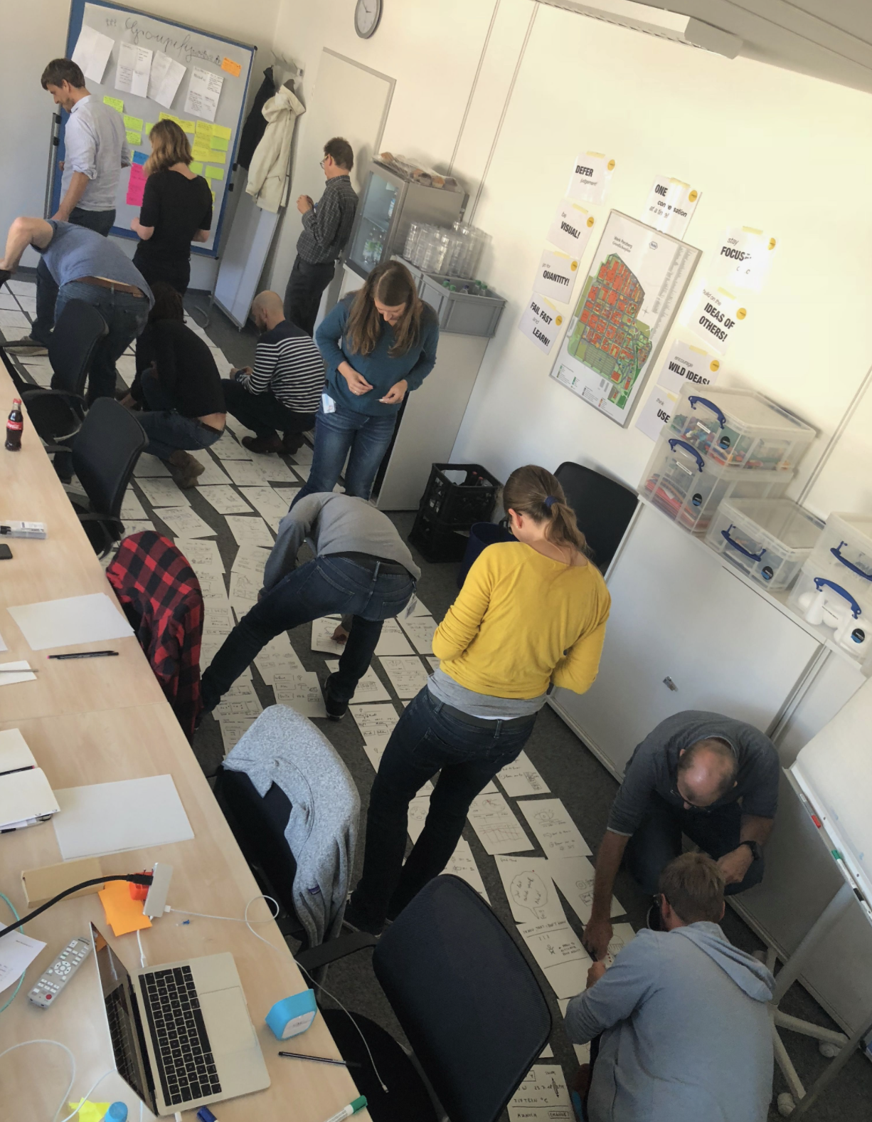 Group of people working together on sticky notes and papers spread on the floor in an office or classroom setting.